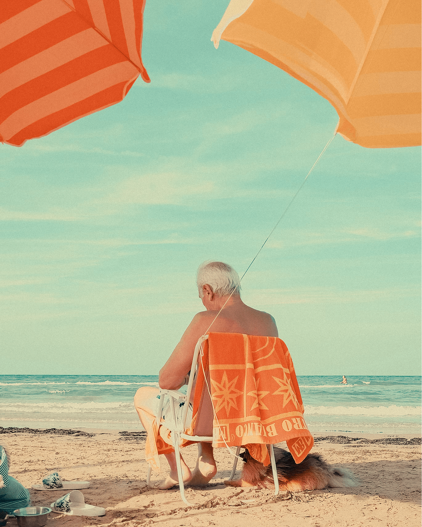 A man under beach umbrellas, watching the sea from his chair