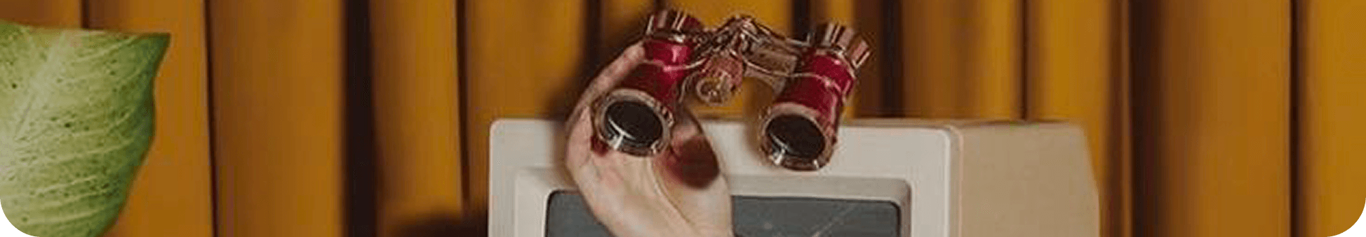 A hand holding opera glasses over a vintage television set